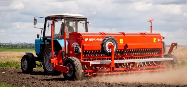 red and blue tractor on green grass field under white clouds during daytime